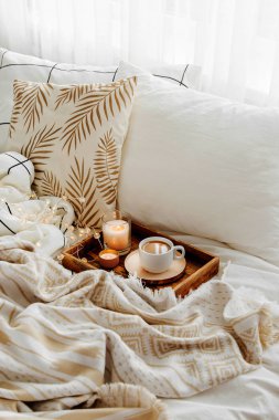 Yatakta ki tahta kahve tepsisi ve mumlar. Çizgili battaniye ve yastık ile beyaz yatak çarşafları. Yatakta kahvaltı. Hygge kavramı.