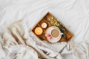 Beyaz yatak üzerinde sıcak ekose ile kahve ve mum tepsisi . Yatakta kahvaltı. İskandinav tarzı. Düz döşeme, üst görünüm