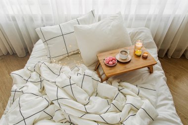 Yatakta ki tahta kahve tepsisi ve mumlar. Çizgili battaniye ve yastık ile beyaz yatak çarşafları. Yatakta kahvaltı. Hygge kavramı.