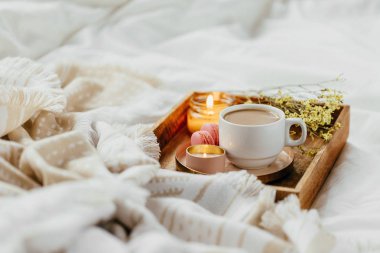 Beyaz yatak üzerinde sıcak ekose ile kahve ve mum tepsisi . Yatakta kahvaltı. İskandinav tarzı. Düz döşeme, üst görünüm