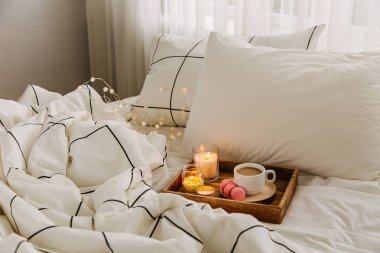 Yatakta ki tahta kahve tepsisi ve mumlar. Çizgili battaniye ve yastık ile beyaz yatak çarşafları. Yatakta kahvaltı. Hygge kavramı.
