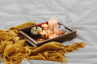 Yatakta sıcak ekose ile ahşap tepsi üzerinde mumlar kabak dekorasyon yanan. Sonbahar stili. Hygge kavramı. 