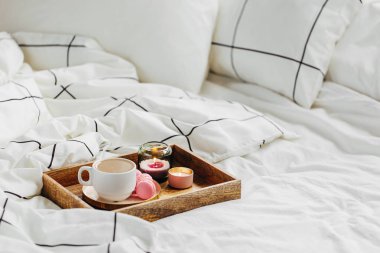 Yatakta ki tahta kahve tepsisi ve mumlar. Çizgili battaniye ve yastık ile beyaz yatak çarşafları. Yatakta kahvaltı. Hygge kavramı.