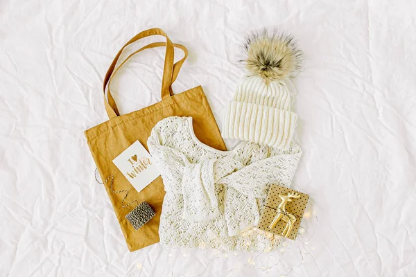 Knitted white sweater with  tote bag and christmas decorations. Winter fashion clothes collage on white background. Top view flat lay.