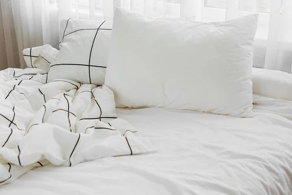 White bedding sheets with striped blanket and pillow. Messy bed.