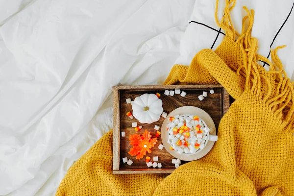 暖かい格子柄のベッドの上にマシュマロとキャンディコーンとコーヒーのカップ 木製のトレイにキャンドルとカボチャを入した秋の飲み物 ヒュッゲコンセプト — ストック写真