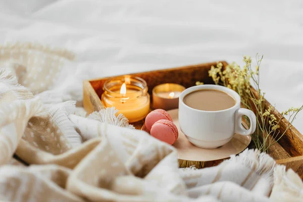 Tray of coffee and candles with warm plaid on white bedding . Breakfast in bed.  Scandinavian style.  Flat lay, top view