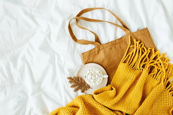 Cotton eco bag with cup of coffee and yellow knitted  scarf on bed. Autumn concept.