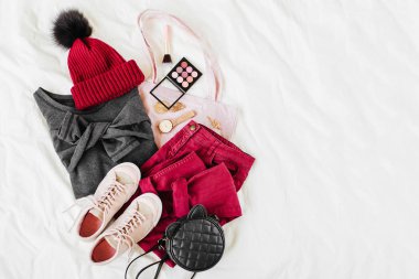 Vinous kış şapka ve gri kazak, çanta ve beyaz levha üzerinde spor ayakkabı ile pantolon. Kadın şık sonbahar veya kış kıyafeti. Modaya uygun giysi kolajı. Düz döşeme, üst görünüm. 