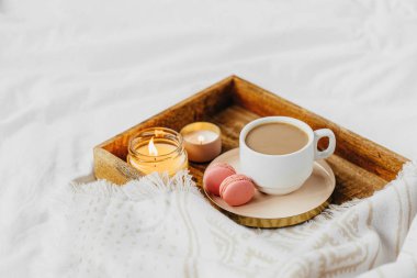 Beyaz yatak üzerinde sıcak ekose ile kahve ve mum tepsisi . Yatakta kahvaltı. İskandinav tarzı. Düz döşeme, üst görünüm