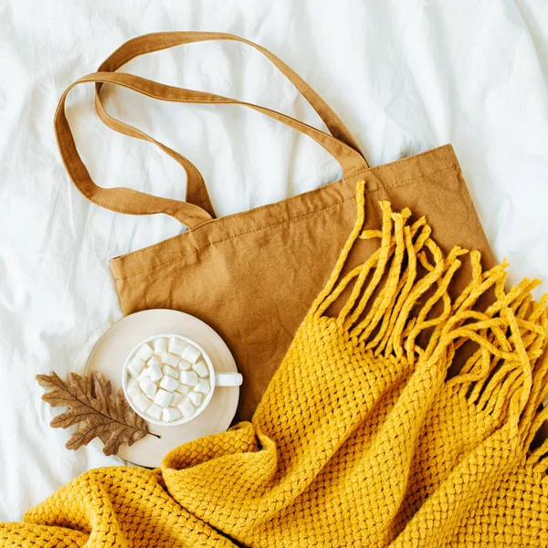 Cotton eco bag with cup of coffee and yellow knitted  scarf on bed. Autumn concept.