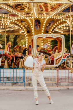 Lunaparkta gece aydınlatmaile carrousel önünde pamuk şeker ile genç kadın. 