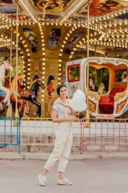 Lunaparkta gece aydınlatmaile carrousel önünde pamuk şeker ile genç kadın. 