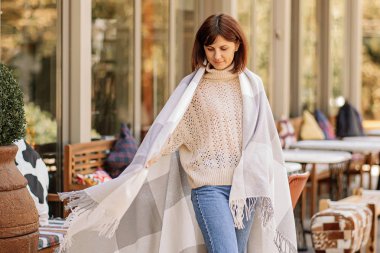 Güzel kız terasta kafede dinleniyor, yünlü ekose battaniye sarılı. Sonbahar sabahı.