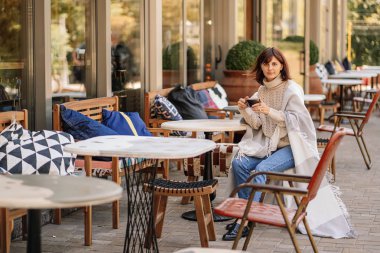 Güzel kız istirahat ve terasta kafede oturan kahve içme, yünlü ekose battaniye sarılı. Sonbahar sabahı.
