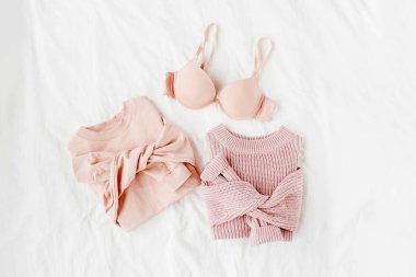Beyaz levha üzerinde sütyen ile soluk pembe sıcak kazak. Kadın şık giysi kolaj. Düz döşeme, üst görünüm. 