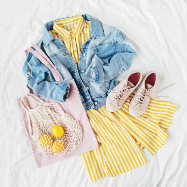 Mavi kot ceket ve eko çanta ve beyaz yatakta spor ayakkabı ile sarı elbise. Kadınların şık sonbahar veya bahar kıyafeti. Modaya uygun kıyafetler. Moda konsepti. Düz döşeme, üst görünüm.