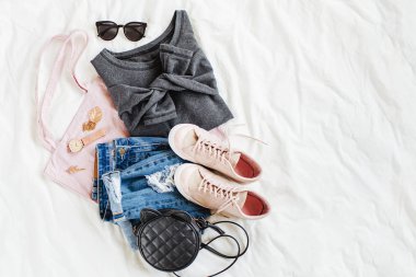 Gri kazak, çanta ve beyaz çarşaf üzerinde spor ayakkabı ile mavi kot pantolon. Kadın şık sonbahar veya kış kıyafeti. Modaya uygun giysi kolajı. Düz döşeme, üst görünüm. 