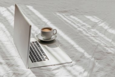 Laptop ve kahve beyaz yatakta. Ev konseptinde çalış. Sabah ışığı 