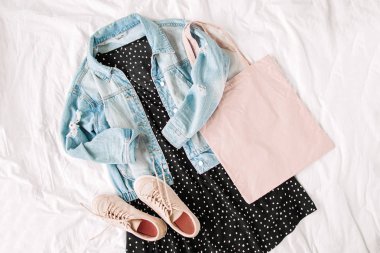 Mavi kot ceket ve beyaz yatakta tote çanta ile siyah elbise. Kadınların şık sonbahar veya bahar kıyafeti. Modaya uygun kıyafetler. Düz döşeme, üst görünüm.