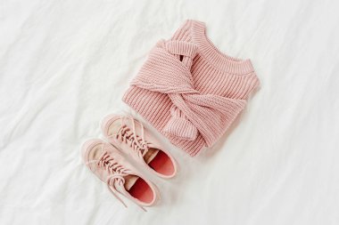 Soluk pembe sıcak kazak ve yatakta spor ayakkabı. Kadın şık sonbahar veya kış lık giysiler. Rahat Kış bakmak. Düz döşeme, üst görünüm.