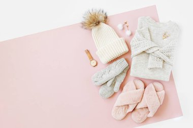 Gri sıcak örgü kazak kış şapka, eldiven ve soluk pembe arka plan üzerinde kabarık kürk terlik ile. Kadınların şık kışlık giysileri. Düz döşeme, üst görünüm.
