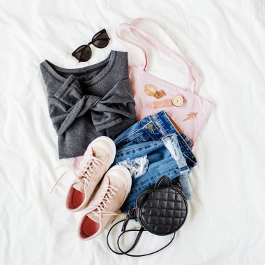 Gri kazak, çanta ve beyaz çarşaf üzerinde spor ayakkabı ile mavi kot pantolon. Kadın şık sonbahar veya kış kıyafeti. Modaya uygun giysi kolajı. Düz döşeme, üst görünüm. 