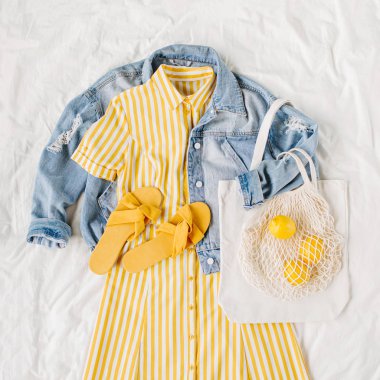 Mavi kot ceket ve beyaz yatakta çanta ve terlik ile sarı elbise. Kadınların şık sonbahar veya bahar kıyafeti. Modaya uygun kıyafetler. Moda konsepti. Düz döşeme, üst görünüm.
