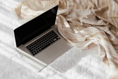 Beyaz yatakta bej ekose dizüstü bilgisayar. Evde çalışma konsepti. Sabah ışığı 