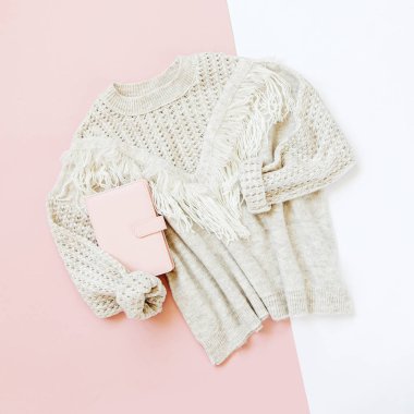 Soluk pembe arka plan kitap ile gri sıcak örme kazak. Kadınların şık kışlık giysileri. Düz döşeme, üst görünüm.