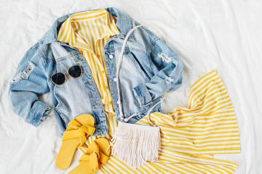 Mavi kot ceket ve beyaz yatakta çanta ve terlik ile sarı elbise. Kadınların şık sonbahar veya bahar kıyafeti. Modaya uygun kıyafetler. Moda konsepti. Düz döşeme, üst görünüm.