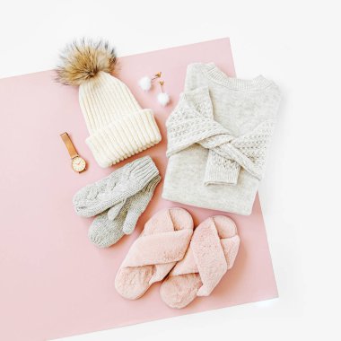 Gri sıcak örgü kazak kış şapka, eldiven ve soluk pembe arka plan üzerinde kabarık kürk terlik ile. Kadınların şık kışlık giysileri. Düz döşeme, üst görünüm.