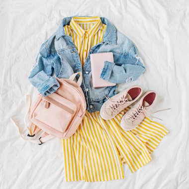 Mavi jean ceket ve sırt çantası, kitap ve beyaz spor ayakkabıları ile Sarı elbise. Kadınların şık sonbahar veya bahar kıyafeti. Üniversite için modaya uygun kıyafetler. Okul konseptine geri dönelim. Düz döşeme, üst görünüm.