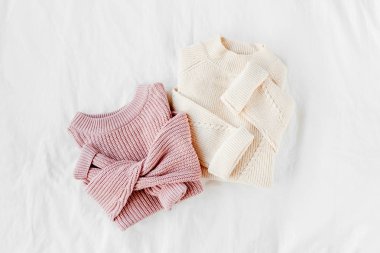 Yatakta soluk pembe ve beyaz sıcak örme kazak. Kadın şık sonbahar veya kış lık giysiler. Düz döşeme, üst görünüm.