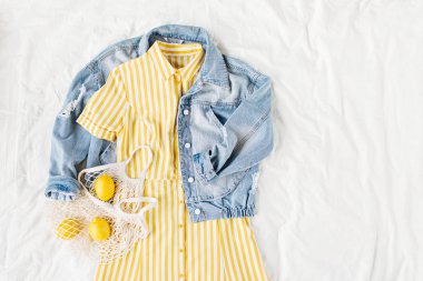 Mavi jean ceket ve beyaz yatakta eko çanta ile Sarı elbise. Kadınların şık sonbahar veya bahar kıyafeti. Modaya uygun kıyafetler. Moda konsepti. Düz döşeme, üst görünüm.