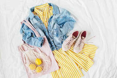 Mavi kot ceket ve eko çanta ve beyaz yatakta spor ayakkabı ile sarı elbise. Kadınların şık sonbahar veya bahar kıyafeti. Modaya uygun kıyafetler. Moda konsepti. Düz döşeme, üst görünüm.