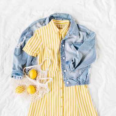 Mavi jean ceket ve beyaz yatakta eko çanta ile Sarı elbise. Kadınların şık sonbahar veya bahar kıyafeti. Modaya uygun kıyafetler. Moda konsepti. Düz döşeme, üst görünüm.