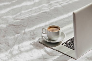 Laptop ve kahve beyaz yatakta. Ev konseptinde çalış. Sabah ışığı 