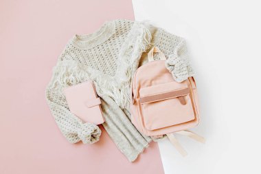 Soluk pembe arka plan üzerinde sırt çantası ile gri sıcak örme kazak. Kadınların şık kışlık giysileri. Düz döşeme, üst görünüm.