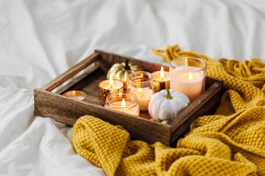 Yatakta sıcak ekose ile ahşap tepsi üzerinde mumlar kabak dekorasyon yanan. Sonbahar stili. Hygge kavramı. 