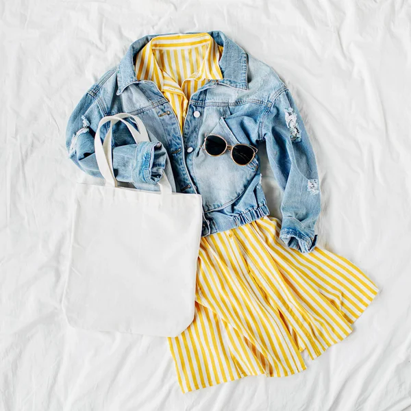 蓝色牛仔裤夹克和黄色连衣裙 白色床上有环保袋 女装时尚的秋季或春季服装 时髦的衣服 时尚理念 顶视图 — 图库照片