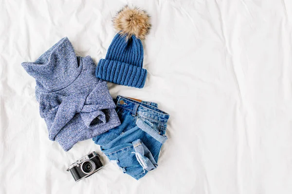 舒适的蓝色毛衣 牛仔裤 帽子和相机在床上的白色床单 女士时尚的秋冬套装 时髦的服装拼贴画 顶视图 — 图库照片