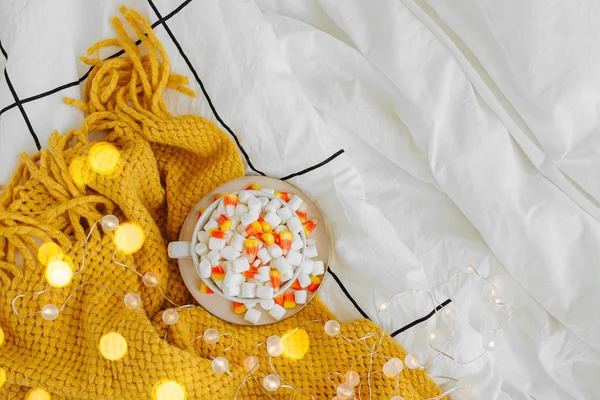 温かいチェック柄のベッドの上にマシュマロとキャンディコーンを入したコーヒー 秋の飲み物 ベッドでの朝食 ヒュッゲコンセプト — ストック写真