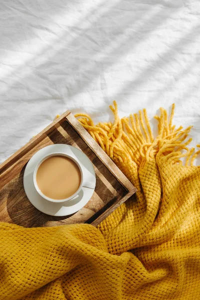 Wooden tray with coffee and warm plaid on white bedding . Breakfast in bed. Hygge concept.