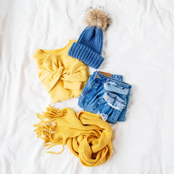 舒适的黄色毛衣 蓝色牛仔裤 围巾和帽子在床上的白床单 女士时尚的秋冬套装 时髦的服装拼贴画 顶视图 — 图库照片