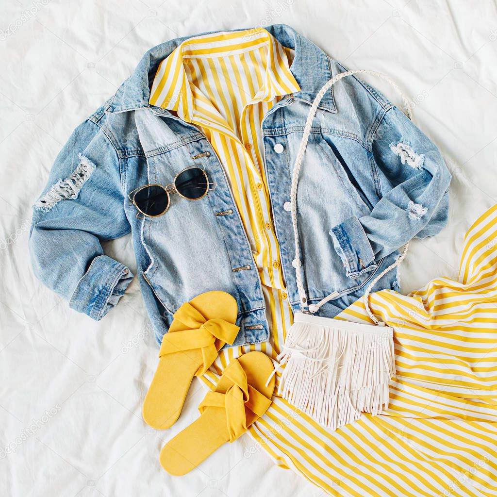 Blue jean jacket and Yellow dress  with  bag and  slippers on white bed. Women's stylish autumn or spring outfit. Trendy clothes. Fashion concept.  Flat lay, top view.