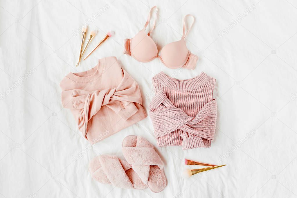 Pale pink warm sweaters with  bra and fluffy fur slippers on white sheet. Women's stylish clothes collage. Flat lay, top view. 