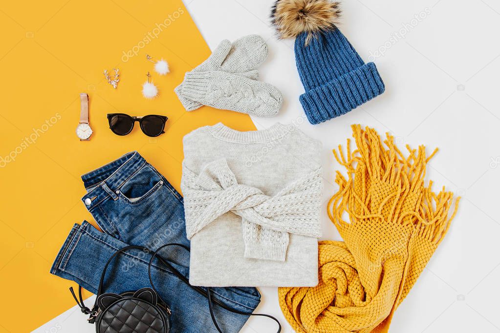 Blue winter hat with jeans, sweater, handbag and yellow scarf on white background. Women's stylish autumn or winter outfit. Trendy clothes collage. Flat lay, top view.
