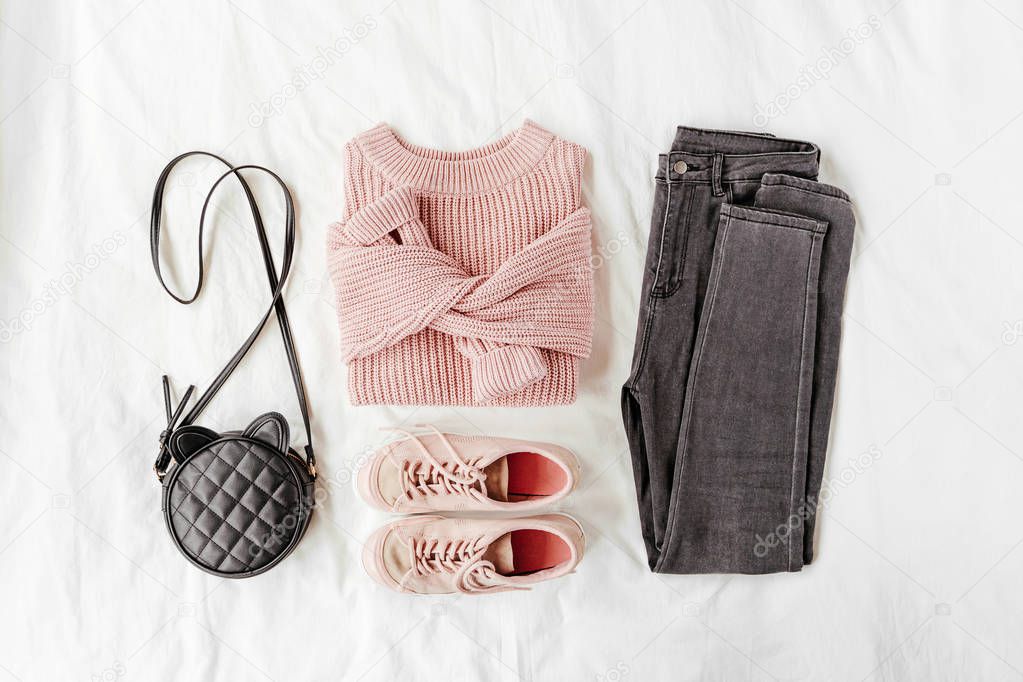 Pale pink warm sweater and gray trousers with sneakers, handbag on white sheet. Women's stylish autumn or winter outfit. Trendy clothes collage. Flat lay, top view. 