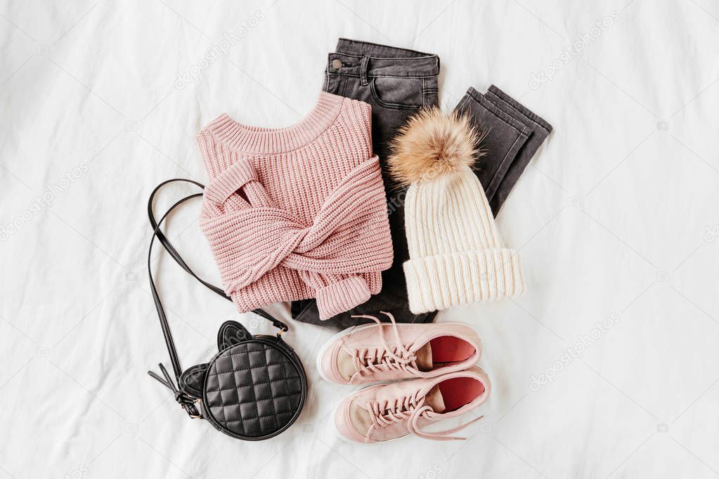 Pale pink warm sweater and gray trousers with sneakers, handbag on white sheet. Women's stylish autumn or winter outfit. Trendy clothes collage. Flat lay, top view. 